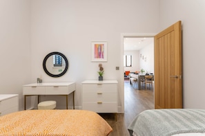 A bedroom with a bed, a bedside table, a mirror, a dresser, and a door leading to a dining area. - Chic 2-Bed Seaside Escape in Vibrant Kemp Town (Brighton and Hove)