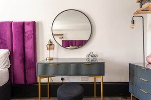 A bedroom with a bed, a vanity with a mirror, a small stool, a dresser, and a lamp. - Fun Kemptown Stay w/ Games Close to the Seafront (Brighton and Hove)