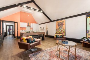 A spacious loft with a high ceiling, a kitchen area, a living room with a sofa and a coffee table, and a large painting on the wall. - Fun Kemptown Stay w/ Games Close to the Seafront (Brighton and Hove)