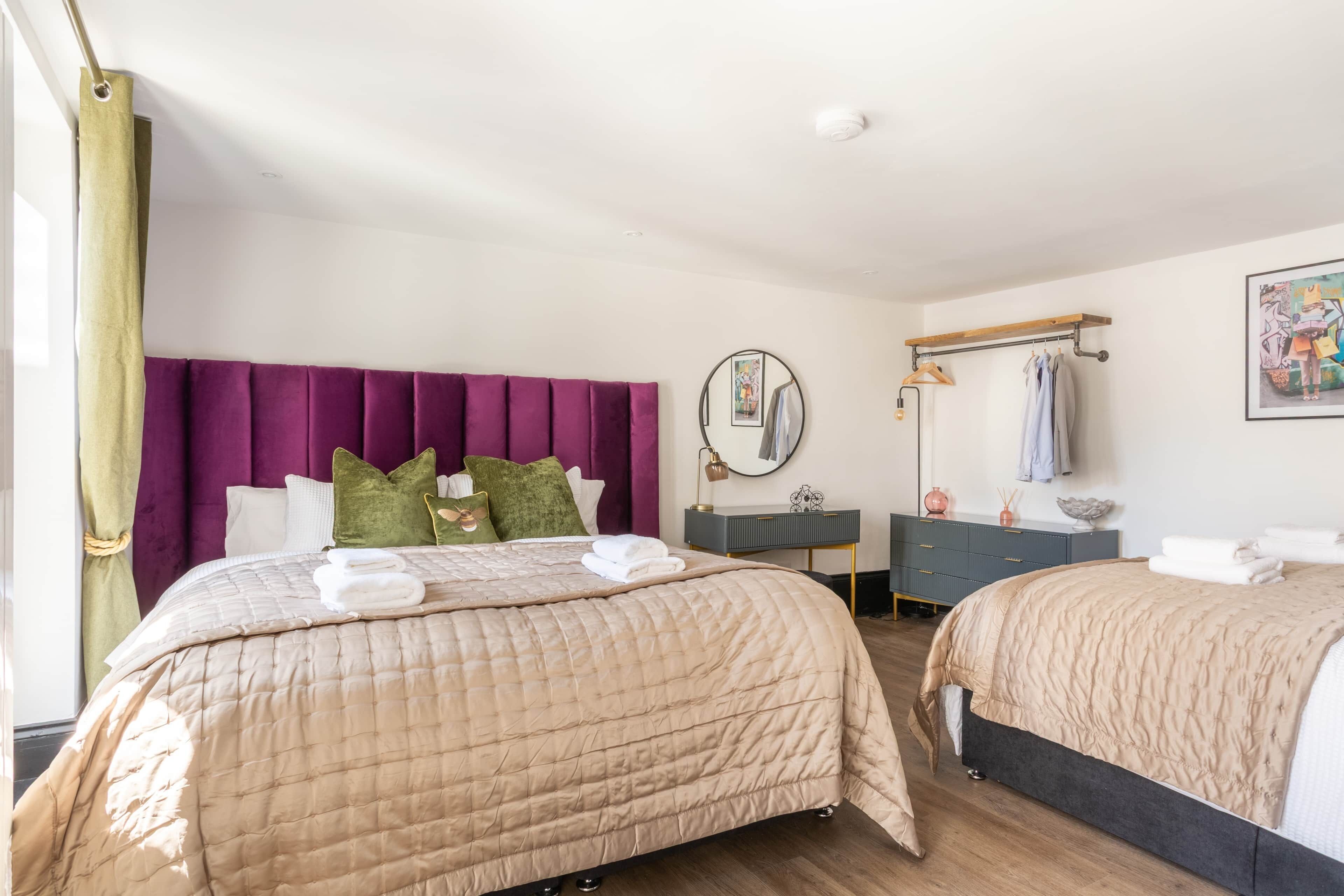 A hotel room with two beds, a vanity, a mirror, and a window with curtains.