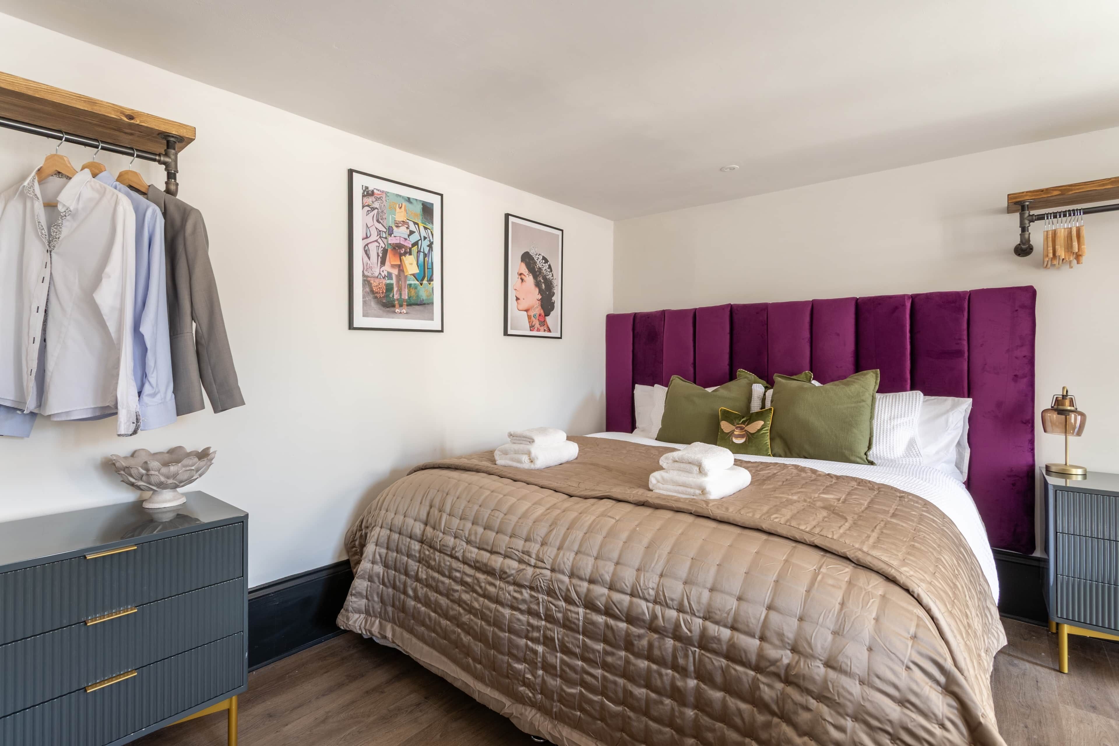 A neatly arranged bedroom with a bed, a dresser, a coat rack, and two framed pictures on the wall.