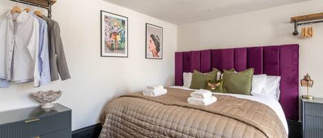 A neatly arranged bedroom with a bed, a dresser, a coat rack, and two framed pictures on the wall.