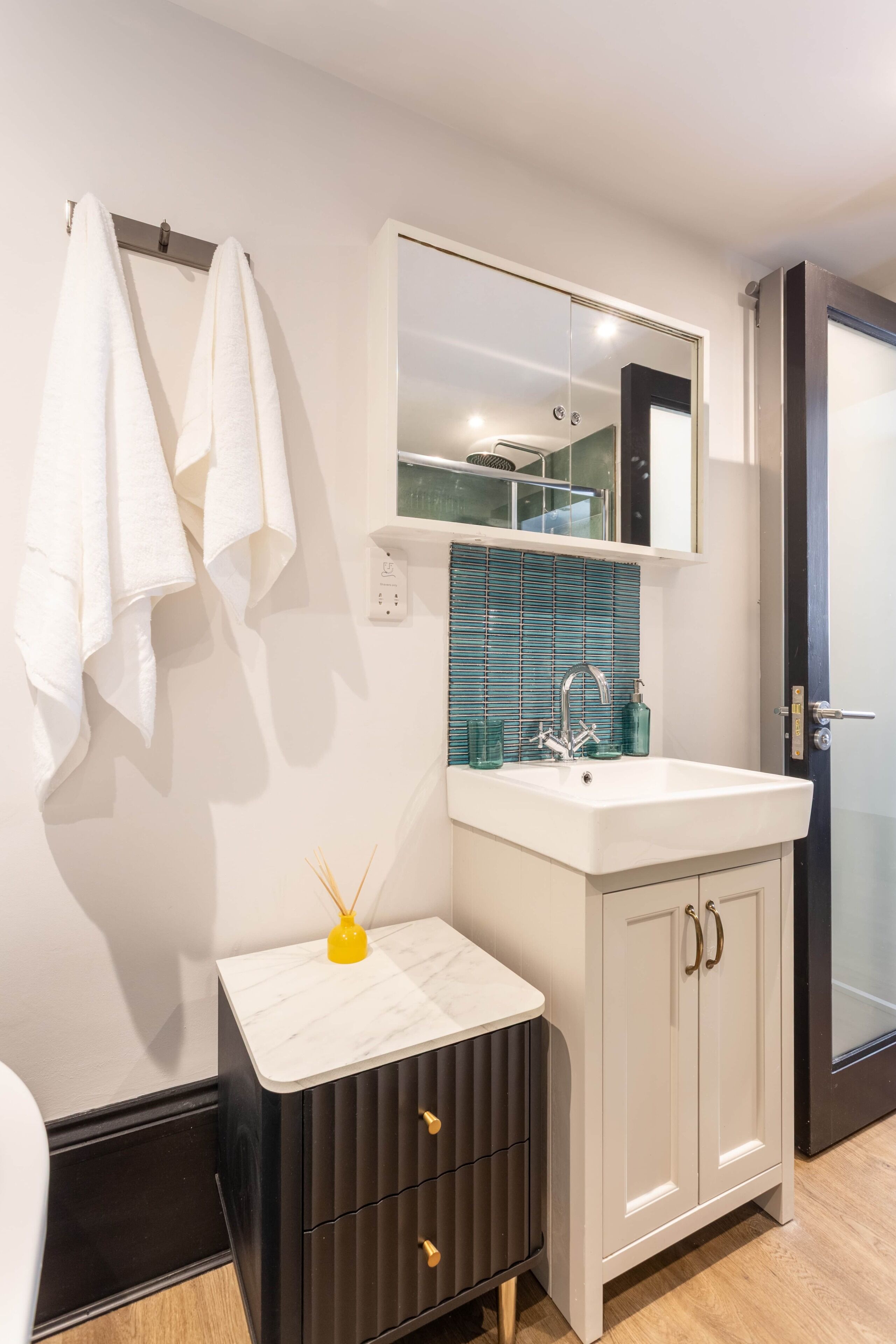 A bathroom with a white sink, a mirror, a towel rack, and a small cabinet with drawers.