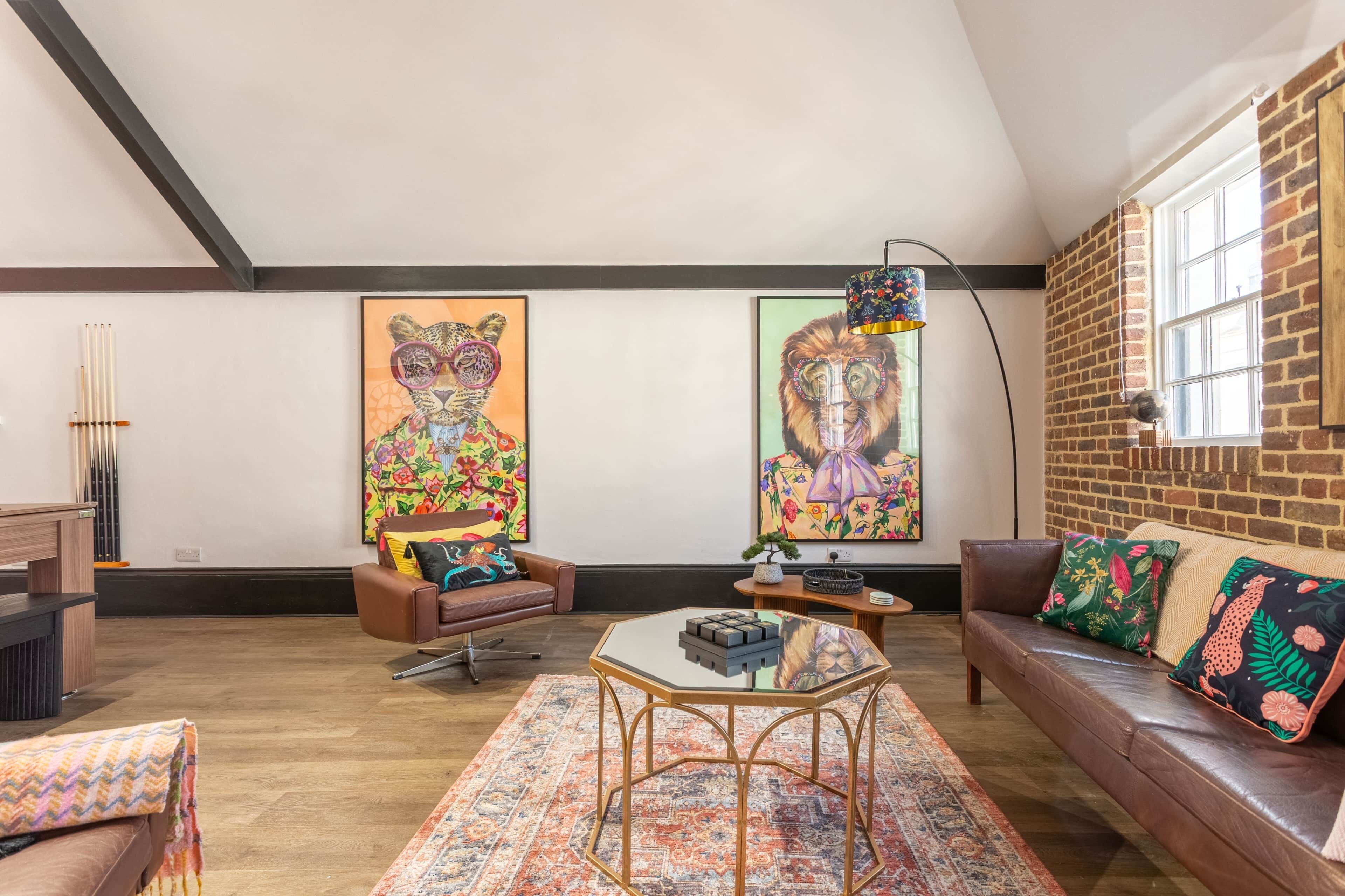 A living room with a brown leather sofa, a glass-top coffee table, a patterned rug, and two large abstract paintings on the wall.