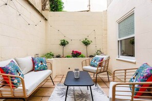 A cozy patio with a sofa, chairs, a small table, and potted plants. - Stylish 2-Bed 2- Bath Seafront Patio Apartment (Brighton and Hove)