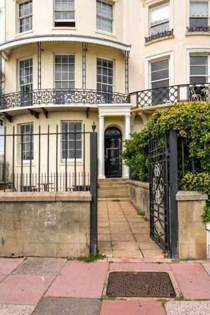 A two-story building with a curved facade, a black iron gate, and a small set of steps leading to the entrance. - Stylish 2-Bed 2- Bath Seafront Patio Apartment (Brighton and Hove)