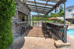 Ein überdachter Außenbereich mit Bar, Steinwänden, Grill und Pool.