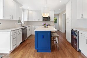 Een moderne keuken met witte kasten, een blauw eiland en een inbouwmagnetron.