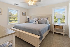 Un dormitorio con cama, mesitas de noche, ventilador de techo y ventanas con persianas.
