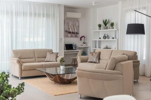 Een moderne woonkamer met twee beige banken, een glazen salontafel en een witte boekenkast met planten en een fiets.