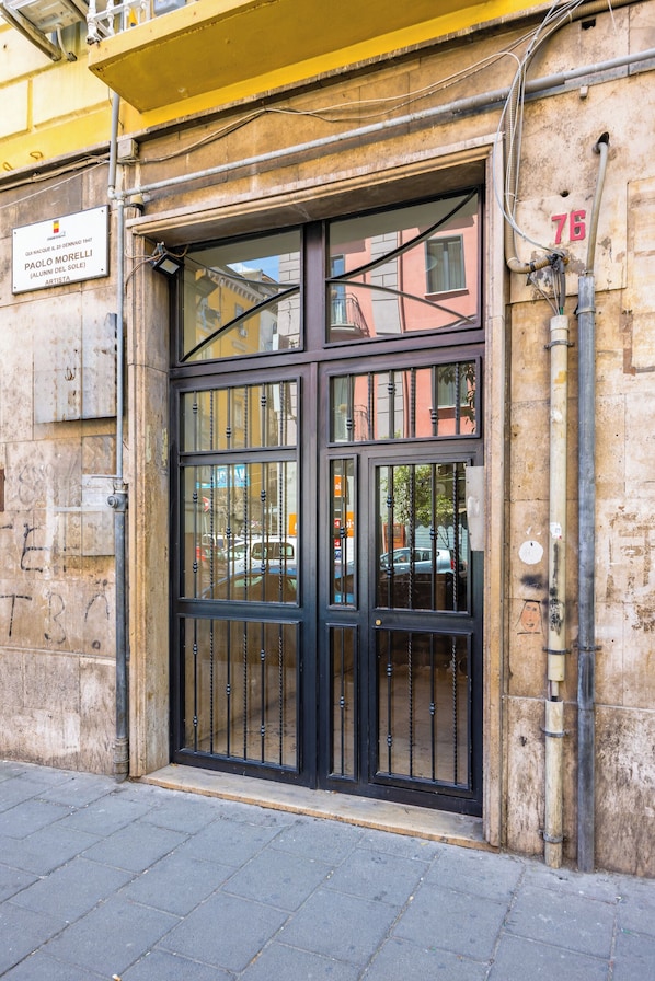 A building entrance with a large black metal gate, a plaque, and a number '76' on the wall. - Urban Retreat 76 (Naples)