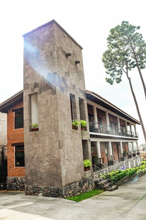 Un edificio con fachada de piedra, un balcón con barandilla y una escalera que conduce a un nivel superior.