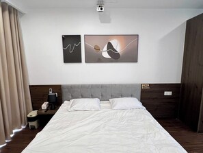Et hotelværelse med en seng, et natbord, en lampe og to abstrakte kunstværker på væggen.