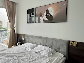 Hotelkamer met een bed, hoofdeinde, nachtkastje, lamp, Wi-Fi signaal en uitzicht op gebouwen door het raam.