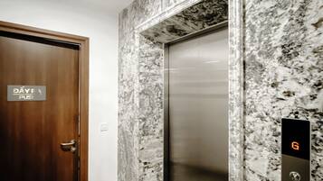 Un ascensor con panel digital, pared de mármol y puerta de madera con un cartel.