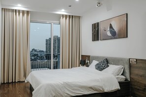A hotel room with a large bed, a view of the city, and a painting on the wall. - Studio Suite Deluxe 35m2 with Balcony (Hà Nội)