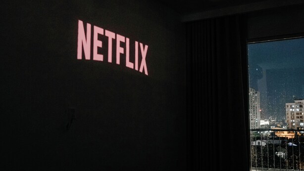 A room with a wall-mounted sign that reads 'NETFLIX' and a view of a cityscape through a window. - Studio Suite Deluxe 35m2 with Balcony (Hà Nội)