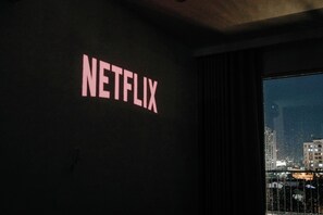 Et værelse med et ophængt skilt der siger 'NETFLIX' og udsigt til bybilledet gennem et vindue.