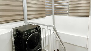 A laundry room with a washer and dryer, a white trash can, and a staircase. - Studio Suite Deluxe 35m2 with Balcony (Hà Nội)