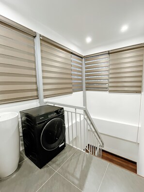 A laundry room with a washer and dryer, a white trash can, and a staircase. - Studio Suite Deluxe 35m2 with Balcony (Hà Nội)