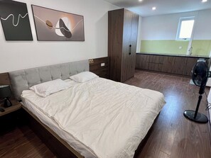 Een slaapkamer met een bed, nachtkastje, kledingkast en een kitchenette op de achtergrond.