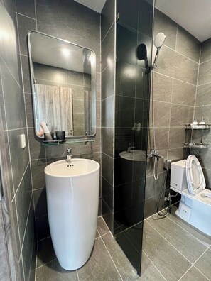 Een moderne badkamer met een groot wit wastafel, een douchecabine van glas en een toilet met een witte deksel.