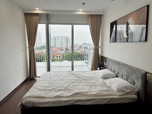 Et hotelværelse med en stor seng, udsigt til bygninger gennem vinduet og en balkon med gelænder.