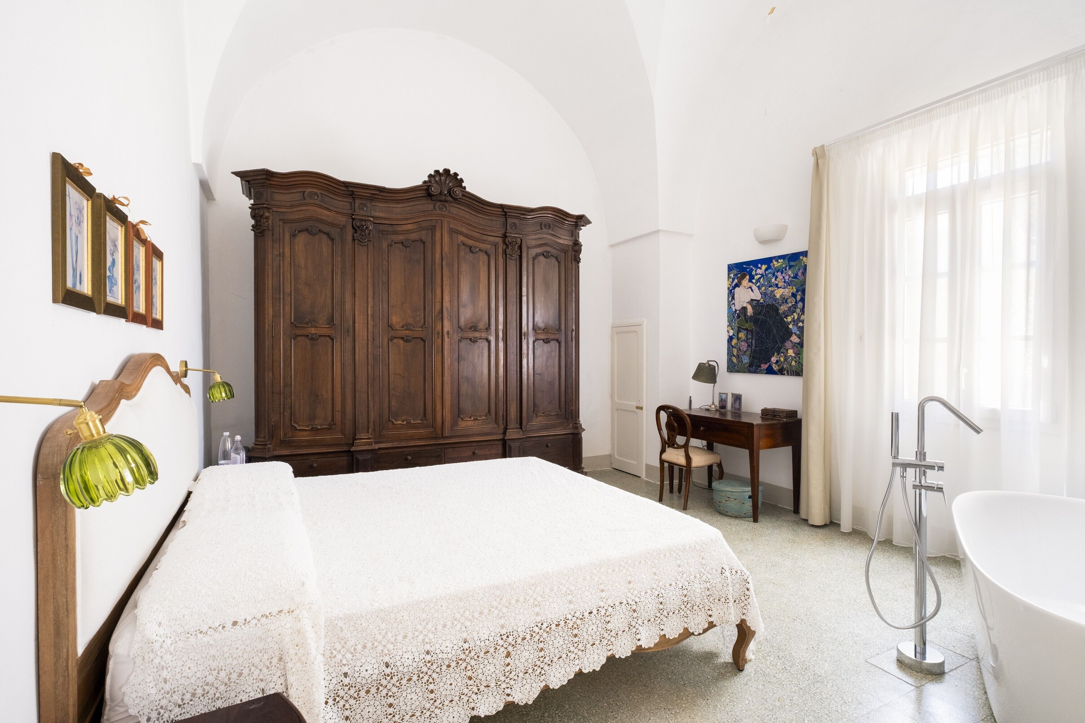 Un dormitorio con cama, un armario de madera, un escritorio con silla, un cuadro, y un baño con bañera.