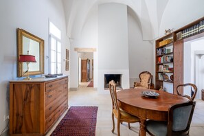 A dining area with a wooden table, chairs, a fireplace, a bookshelf, and a mirror on the wall.