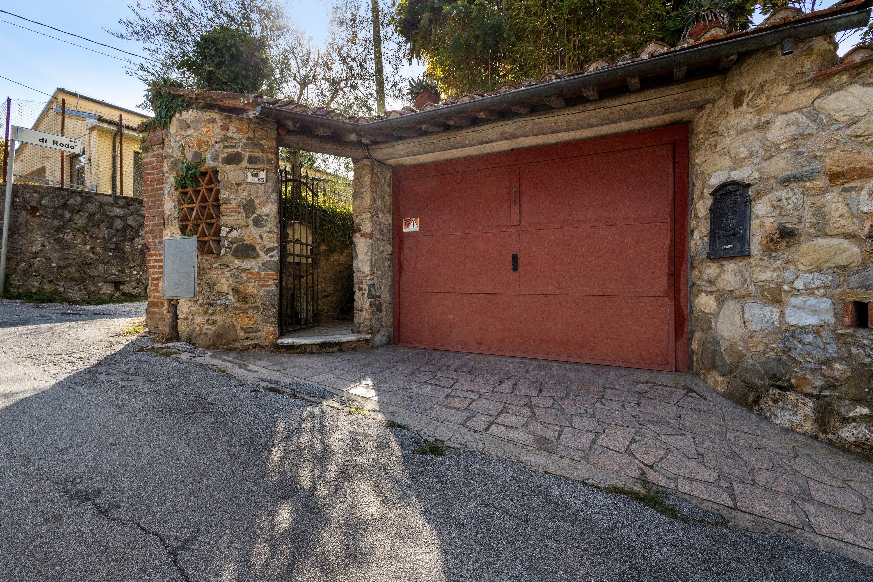 A stone building with a red garage door, a metal gate, and a stone wall with a number plaque.