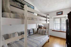 Een slaapkamer met een stapelbed, een raam, een houten vloer en een wandplank met een mand.