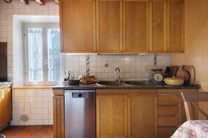 Een keuken met houten kastjes, een dubbele spoelbak, een vaatwasser en een raam met gordijnen.