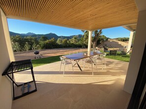 Eine überdachte Terrasse mit Tisch, Stühlen, einem Grill und Blick auf die Berge.