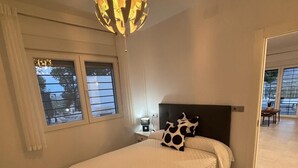 Ein Schlafzimmer mit einem Bett, einem Nachttisch, einer Lampe, einem Fenster und einer Tür zu einem anderen Raum.