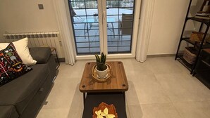 Ein Wohnzimmer mit Sofa, einem Couchtisch mit Pflanze und Blick durch eine Glastür.
