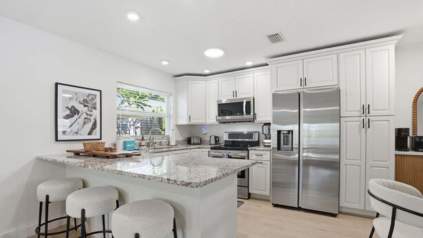 A modern kitchen with white cabinets, stainless steel appliances, a granite countertop, and bar stools. - The Full Florida Experience -Pool, Bikes and Beach (Naples)
