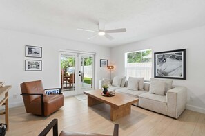 Ein Wohnzimmer mit braunem Ledersessel, beigem Sofa, Couchtisch aus Holz und Deckenventilator.