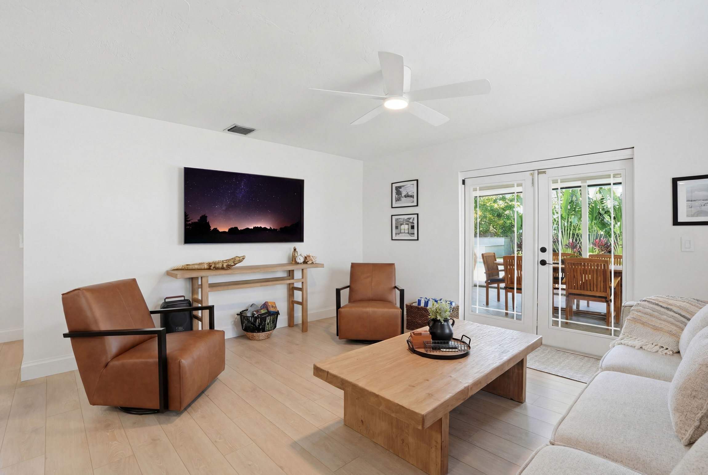 Een moderne woonkamer met een houten salontafel, twee leren fauteuils, een plafondventilator en een schuifdeur naar een buitenruimte.