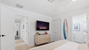 A bedroom with a bed, a dresser, a television, and a surfboard. - The Full Florida Experience -Pool, Bikes and Beach (Naples)