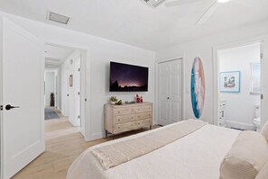 Ein Schlafzimmer mit einem Bett, einem Schminktisch, einem Fernseher und einem Surfbrett.
