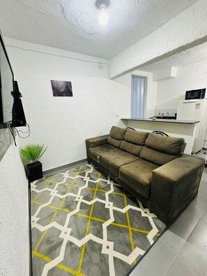 A compact living space with a sofa, a small kitchen area, and a patterned rug. - Vrbo Property (São Paulo)