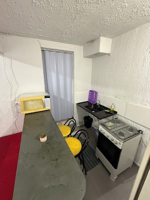 Ett kompakt kök med mikrovågsugn, spis och ett litet matbord med gula stolar.