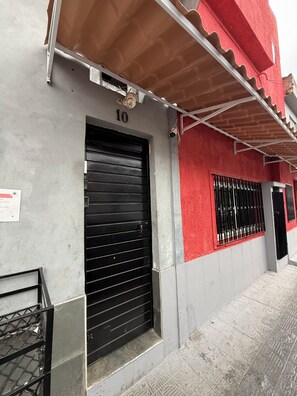 A building with a closed black shutter door, a number '10' above it, and a red and grey facade. - Furnished 1-Bedroom Apartment in the North Zone (São Paulo)