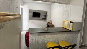 Una cocina compacta con microondas, un televisor pequeño y dos taburetes amarillos.