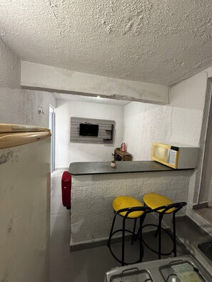 A compact kitchen with a microwave, a small TV, and two yellow bar stools. - Furnished 1-Bedroom Apartment in the North Zone (São Paulo)