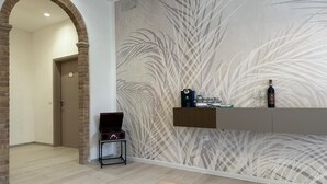 A modern hotel lobby with a brick archway, a wooden bench, a wall-mounted shelf with a bottle and glasses, and a patterned wallpaper. - Villa BRUNI Wine Guest House (Montefalco)