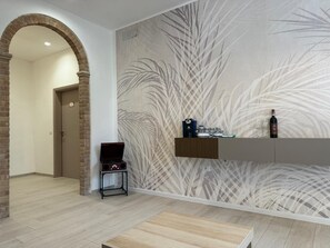 A modern hotel lobby with a brick archway, a wooden bench, a wall-mounted shelf with a bottle and glasses, and a patterned wallpaper. - Villa BRUNI Wine Guest House (Montefalco)
