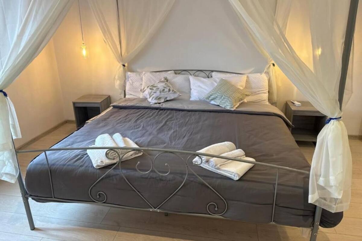 A four-poster canopy bed with a metal frame, white bedding, and a bedside table with a lamp.
