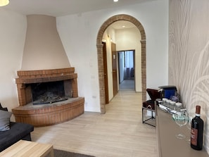 A living room with a brick fireplace, a sofa, a coffee table, and a wine bottle on a counter. - Villa BRUNI Wine Guest House (Montefalco)