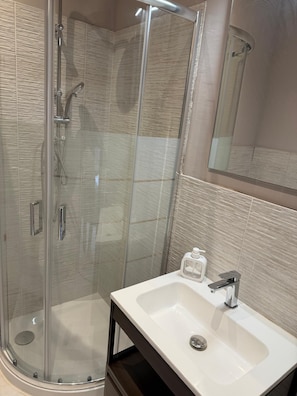 Un baño moderno con ducha envuelta en vidrio, un lavamanos blanco y un espejo sobre él.